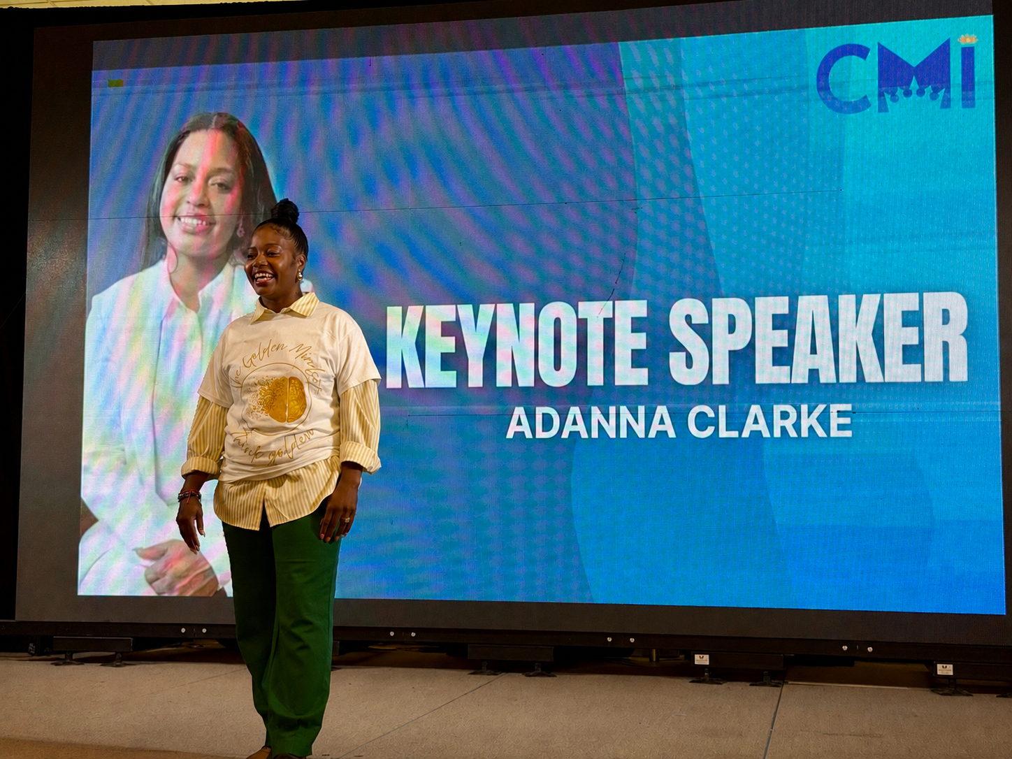 Adanna Clarke on stage as keynote speaker with her image projected behind her